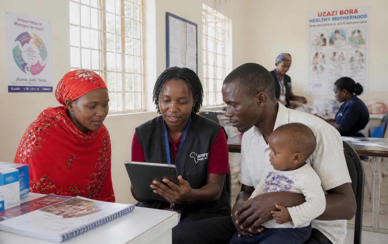 AAHRED health workers reviewing digital health records with a family in an East African clinic